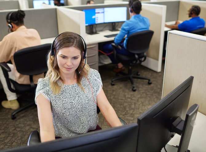ADT customer service rep in the ADT call center typing on her computer and troubleshooting with a customer on her headset 